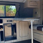 VW Transporter with side door open, showing kitchen, bed, tables and curtains